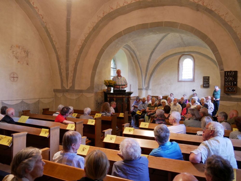 Kirche mit vielen Menschen in Bänken und Mann auf der Kanzel. 