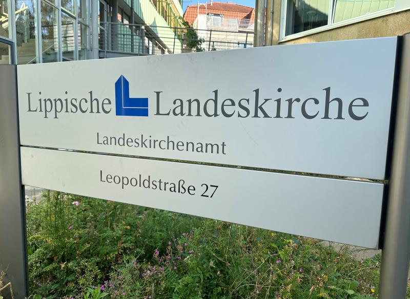 Eingangsbereich des Landeskirchenamtes. Im Hintergrund Gebäude, im Vordergrund ein Schild mit der Aufschrift Lippische Landeskirche. 